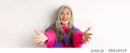 Close-up of stylish asian mature woman reaching hands forward, stretching arms for hug or hold something, smiling happy, standing over white background Close-up of stylish asian mature woman reaching hands forward, stretching arms for hug or hold something, smiling happy, standing over white background 98918439