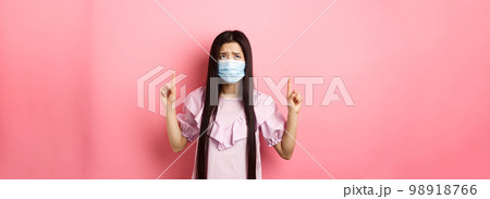 Coronavirus, quarantine and lifestyle concept. Disappointed sad asian girl pointing fingers up, frowning and sulking at unfair situation, standing against pink background Coronavirus, quarantine and lifestyle concept. Disappointed sad asian girl pointing fingers up, frowning and sulking at unfair situation, standing against pink background 98918766