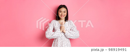 Beautiful asian woman thanking you, holding hands together in appreciation gesture, smiling happy at camera, standing grateful over pink background Beautiful asian woman thanking you, holding hands together in appreciation gesture, smiling happy at camera, standing grateful over pink background 98919491