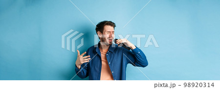 Romantic guy singing song in microphone and gesture, singer playing karaoke, standing on blue background 98920314
