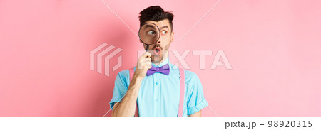Surprised man saying wow and look aside through magnifying glass, checking out promo offer, standing over pink background 98920315