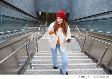 Outdoor shot of young woman plans route, follows map on smartphone app, goes up stairs with backpack and smiles 98920676