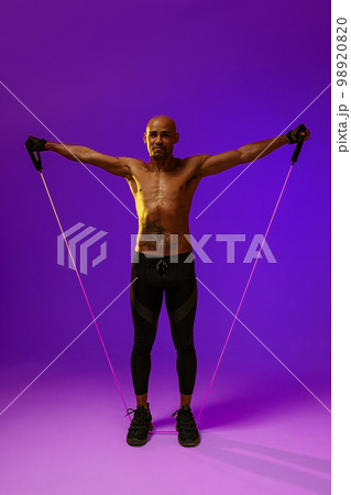 Sporty man performs exercises with expander on studio background. Strength and motivation 98920820