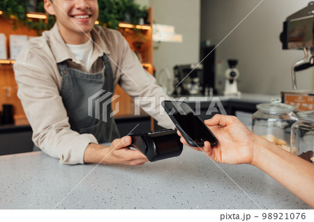 Unrecognizable cafe owner holding card machine at the counter while customer making payment by smartphone Unrecognizable cafe owner holding card machine at the counter while customer making payment by smartphone 98921076
