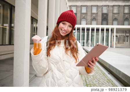 Stylish ginger girl, tourist walks with digital tablet around city, woman connects to iternet on her gadget, looking up information, texting message Stylish ginger girl, tourist walks with digital tablet around city, woman connects to iternet on her gadget, looking up information, texting message 98921379