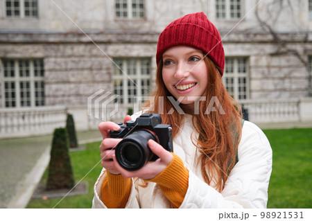 Happy redhead girl tourist, takes photos, photographer with professional camera walks around city and captures beautiful pictures 98921531