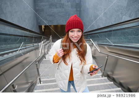 Portrait redhead girl tourist, goes up stairs with smartphone, follows route on mobile phone app, holds backpack and smiles 98921986