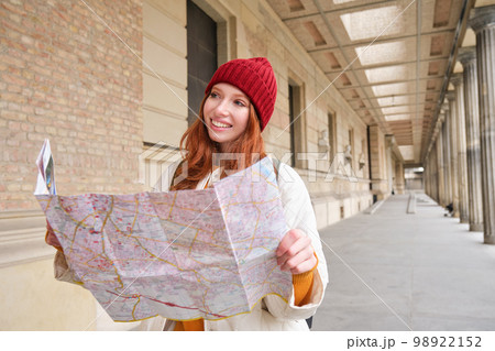 Smiling young redhead woman in red hat, looks at paper map to look for tourist attraction. Tourism and people concept. Girl explores city, tried to find way Smiling young redhead woman in red hat, looks at paper map to look for tourist attraction. Tourism and people concept. Girl explores city, tried to find way 98922152