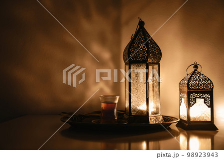 Arabic lantern glowing at night. Dark background, ornamental golden shadows. Festive greeting card, invitation. Muslim holy month Ramadan Kareem. Turkish tea. Eid ul Fitr, Eid ad Adha. Iftar dinner. 98923943