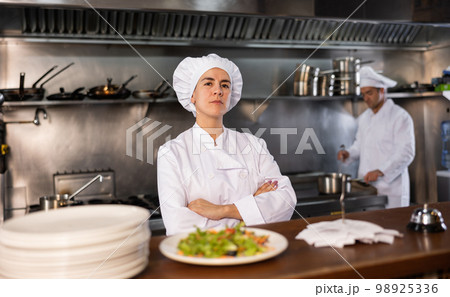 Portrait of female chef with crossed arms along with team of cooks in kitchen of restaurant 98925336