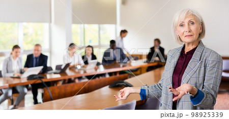 Elegant senior white businesswoman posing with welcoming hand gesture Elegant senior white businesswoman posing with welcoming hand gesture 98925339