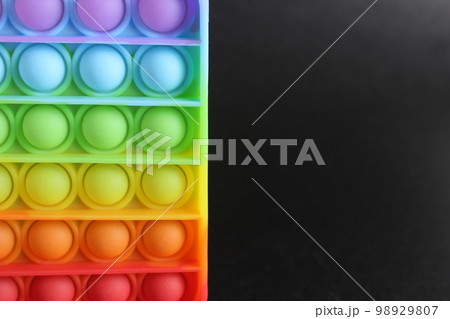 Multi-colored anti-stress toy square and spinner popit simple dimple on a black background with space for text and with copyspace 98929807