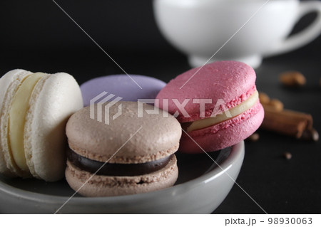Macaroons on a gray plate at the back stands a cup of coffee or tea coffee beans and cinnamon sticks on a black background with a place for text and with a copyspace Macaroons on a gray plate at the back stands a cup of coffee or tea coffee beans and cinnamon sticks on a black background with a place for text and with a copyspace 98930063