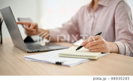 A businesswoman working at her desk, using laptop and taking notes on her notepad. A businesswoman working at her desk, using laptop and taking notes on her notepad. 98930285