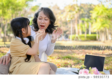 An adorable cute Asian little granddaughter sharing doughnut to her grandmother An adorable cute Asian little granddaughter sharing doughnut to her grandmother 98930773