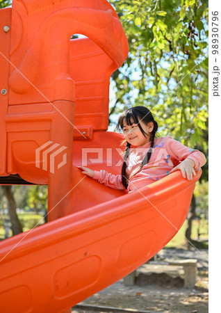 Joyful and happy little Asian girl playing on slider, enjoying outdoor activity. 98930796