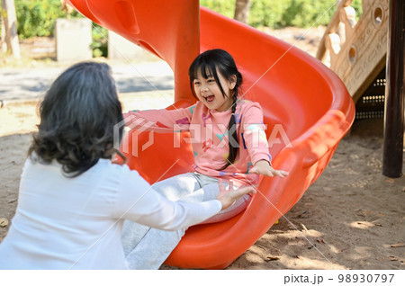 Happy Asian little girl playing on slider, enjoys playing on playground with her grandmother 98930797