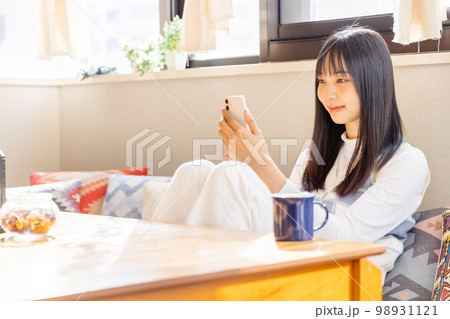 ローソファーに座りスマートフォンを使う若い女性 98931121