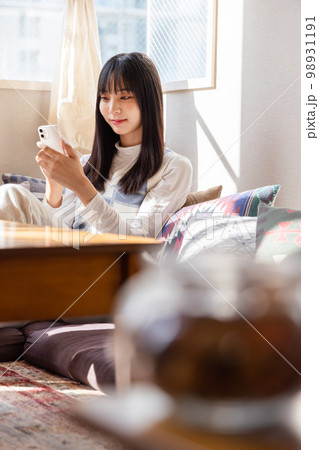 ローソファーに座りスマートフォンを使う若い女性 98931191