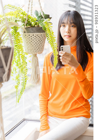 窓辺に座りスマートフォンを使う若い女性 98931323