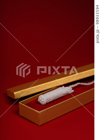 Women's hygienic tampon in a golden gift box on a red background. 98933594
