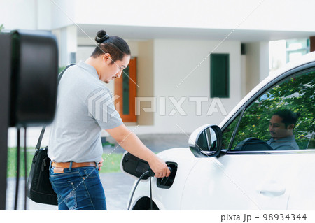 Progressive asian man recharge his EV car at home charging station. 98934344