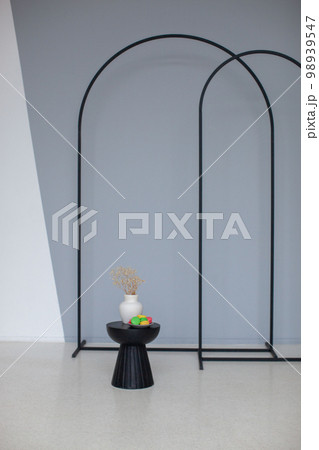 Interior metal arch in black color. Chair and vase with macaroons. Interior metal arch in black color. Chair and vase with macaroons. 98939547