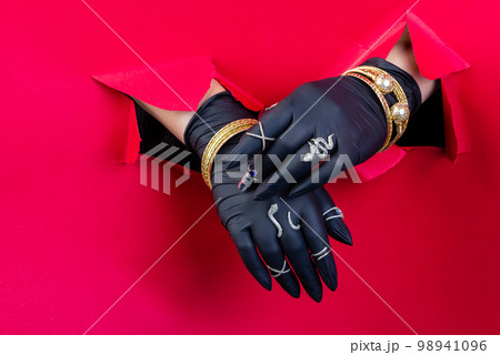 Black gloved hands with expensive jewelry accessories. Breaking through a red paper wall. 98941096