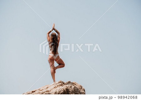 Woman sea yoga. Back view of free calm bliss satisfied woman with long hair standing on top rock with yoga position against of sky by the sea. Healthy lifestyle outdoors in nature, fitness concept. 98942068