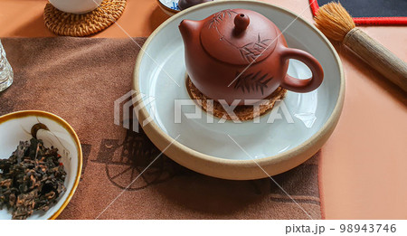 Tea ceremony. Chinese pu-erh in a bowl. In the background is a brown teapot and tea leaves. 98943746