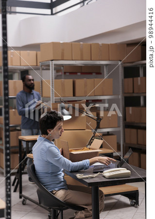 Woman supervisor looking at cargo stock on laptop computer while checking fashion blouse status before start preparing clients packages. Employee working at warehouse delivery department Woman supervisor looking at cargo stock on laptop computer while checking fashion blouse status before start preparing clients packages. Employee working at warehouse delivery department 98944416