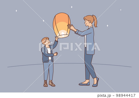 Teenage boy together with older sister launch air fire lantern standing on street under starry sky 98944417