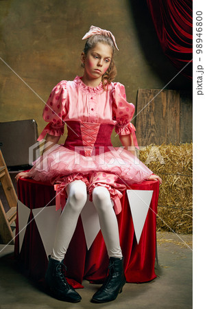 Beautiful little girl in festive pink dress posing with sad emotions over dark vintage circus background. Holidays, dreams, art, fashion, vintage style Beautiful little girl in festive pink dress posing with sad emotions over dark vintage circus background. Holidays, dreams, art, fashion, vintage style 98946800