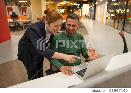 A red-haired Caucasian woman stands at the desktop of a bearded man. The boss approves the work of the subordinate.  98947149