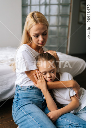 Vertical portrait of loving caring young mother comforting offended sad little daughter lying with closed eyes showing love and care, expressing support, hugging on floor. Family bonding concept. Vertical portrait of loving caring young mother comforting offended sad little daughter lying with closed eyes showing love and care, expressing support, hugging on floor. Family bonding concept. 98948479