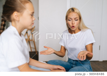 Closeup side view of furious emotional young blonde mom scolding, raising voice, scream and gesturing with hands at stubborn difficult little child daughter at home. Concept of mother-children problem Closeup side view of furious emotional young blonde mom scolding, raising voice, scream and gesturing with hands at stubborn difficult little child daughter at home. Concept of mother-children problem 98948486