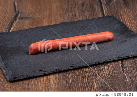 Thin unpeeled semi-smoked sausage on a stone serving board. 98948501