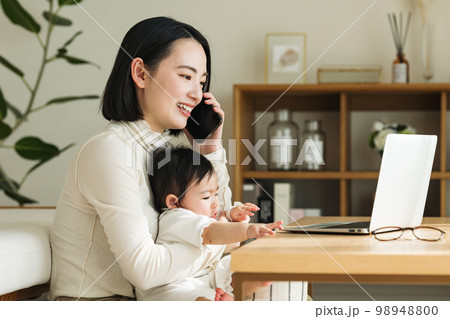赤ちゃんを抱っこしながらスマホで話す女性 98948800