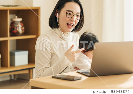 赤ちゃんを抱っこしながらパソコンで話す主婦 赤ちゃんを抱っこしながらパソコンで話す主婦 98948874