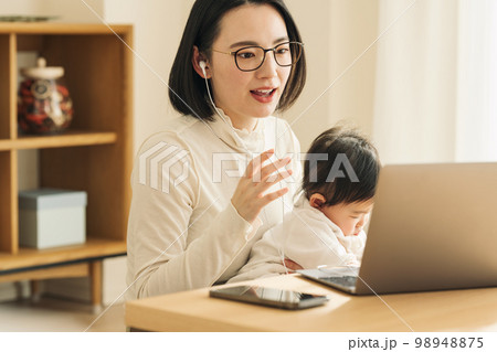 赤ちゃんを抱っこしながらパソコンで話す主婦 赤ちゃんを抱っこしながらパソコンで話す主婦 98948875
