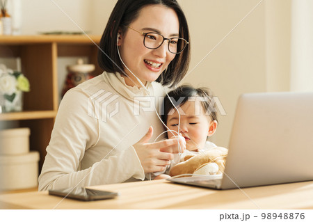 赤ちゃんを抱っこしながらパソコンで話す主婦 98948876