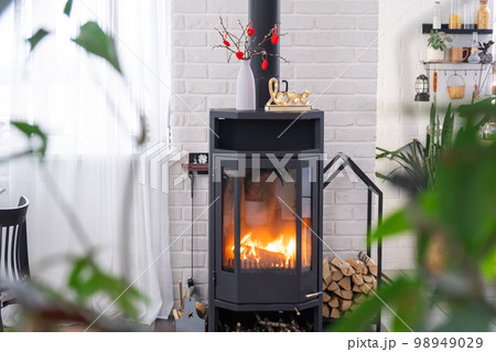 Valentine decor near fireplace stove with fire and firewood. Cozy home hearth in interior with potted plans, valentines day in family love nest. Valentine decor near fireplace stove with fire and firewood. Cozy home hearth in interior with potted plans, valentines day in family love nest. 98949029