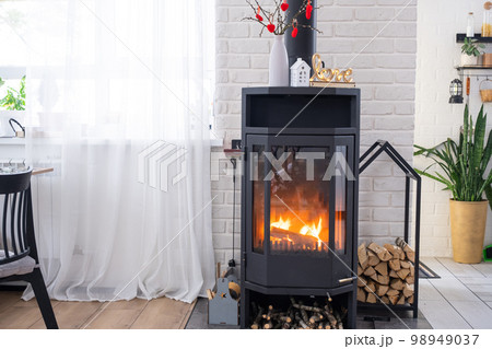 Valentine decor near fireplace stove with fire and firewood. Cozy home hearth in interior with potted plans, valentines day in family love nest. Valentine decor near fireplace stove with fire and firewood. Cozy home hearth in interior with potted plans, valentines day in family love nest. 98949037