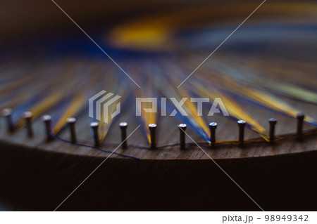 Colored thread mandala on a wooden board with nails. Mandala Moon Harmony Sun esotericism and psychology pictures from yellow and blue silk threads. 98949342