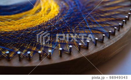 Colored thread mandala on a wooden board with nails. Mandala Moon Harmony Sun esotericism and psychology pictures from yellow and blue silk threads. 98949343
