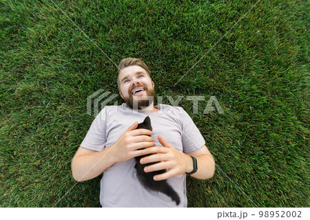 Man with little kitten lying and playing on grass - friendship love animals and pet owner concept Man with little kitten lying and playing on grass - friendship love animals and pet owner concept 98952002