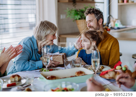 Grandmother giving gift to her granddaughter during Easter dinner. 98952259