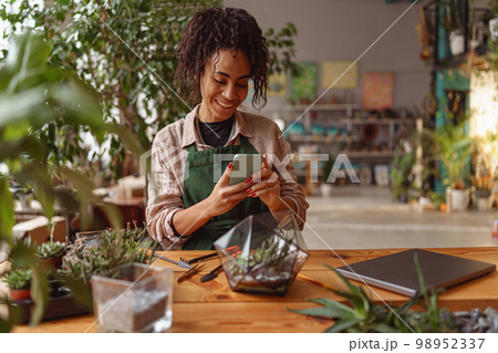 Smiling woman florist taking picture with her plants for publishing in social media Smiling woman florist taking picture with her plants for publishing in social media 98952337