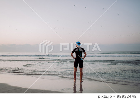 Rear view of woman in neoprene entering in to ocean. 98952448