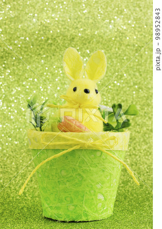 Funny rabbit with a carrot in a basket with flowers. Lovely easter toy. Greeting card for Easter. Vertical orientation Funny rabbit with a carrot in a basket with flowers. Lovely easter toy. Greeting card for Easter. Vertical orientation 98952843